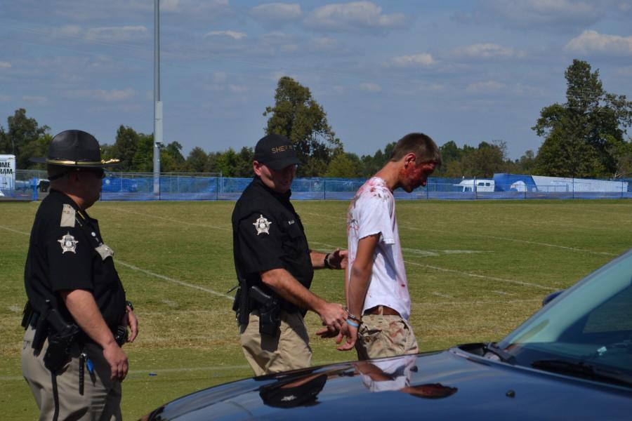 ACCIDENT SIMULATION-- Senior Daniel Pirtle is handcuffed and escorted to a Graves County Sherriffs cruiser, after the character he played was drinking and showing off for the girls on an ATV, causing a fatal accident.