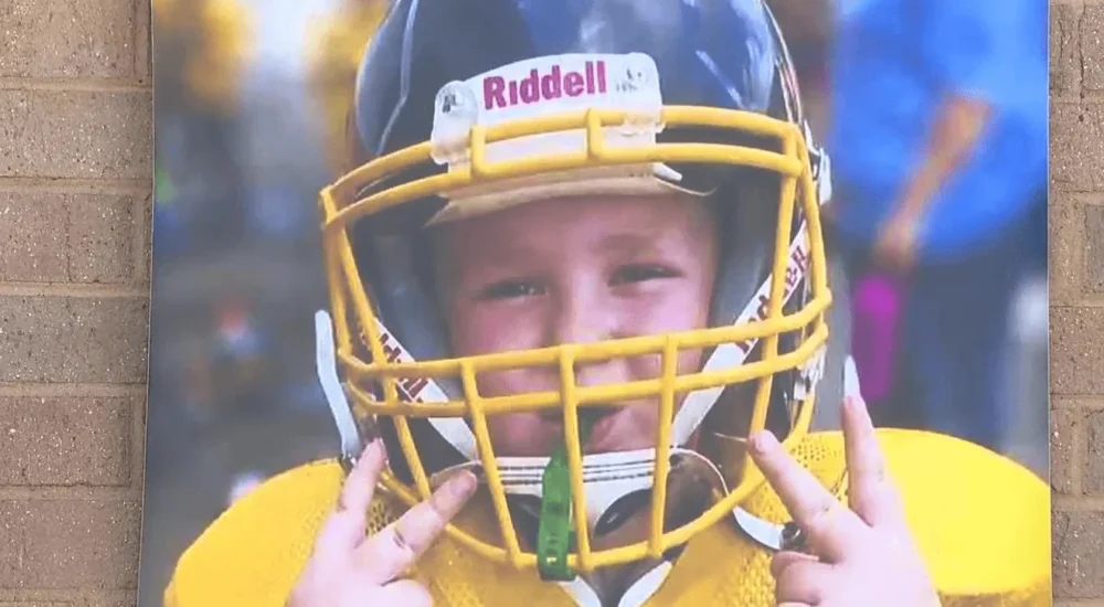 Youth football players in West Virginia honor a teammate with helmet decals and supportive socks