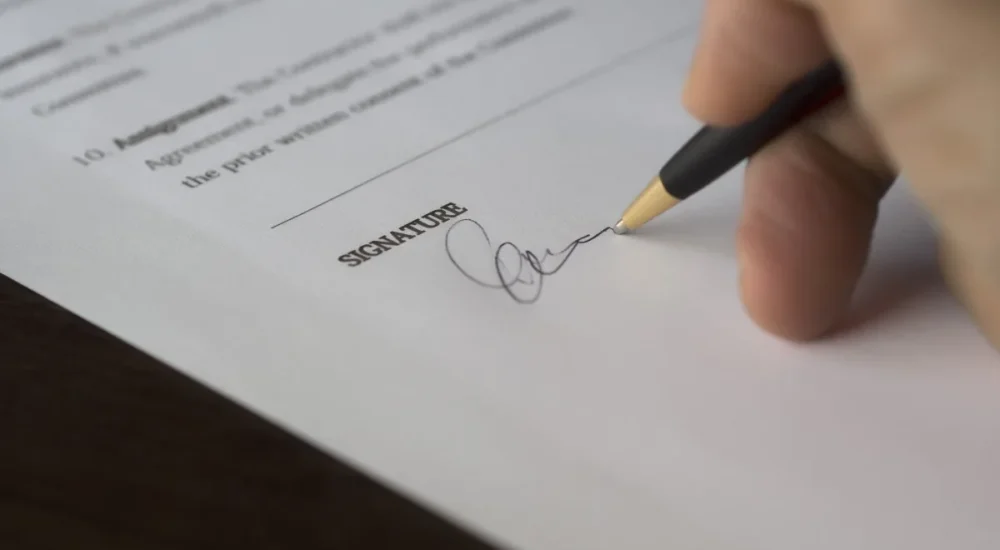 A person signs a contract at a desk, symbolizing an alleged forged employment document